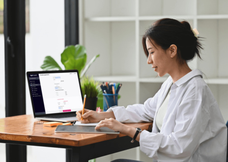 Woman writing a note whilst sitting in front of a laptop with a Tyro Health Online Payments Plan screen.