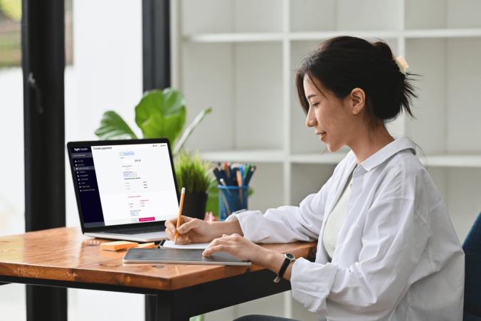 Woman writing a note whilst sitting in front of a laptop with a Tyro Health Online Payments Plan screen.